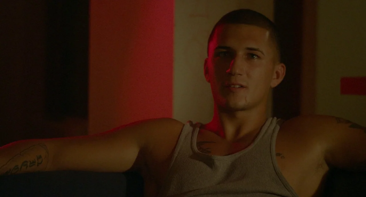 It Felt Like Love (2013) movie still: medium — A dimly lit room provides the backdrop for a close framing of a man. The man is sitting back on a…