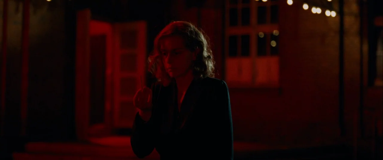 Phoenix (2014) movie still: medium — A woman stands on a darkened patio at night lit by a red source. She holds a small, light-colored object toward…