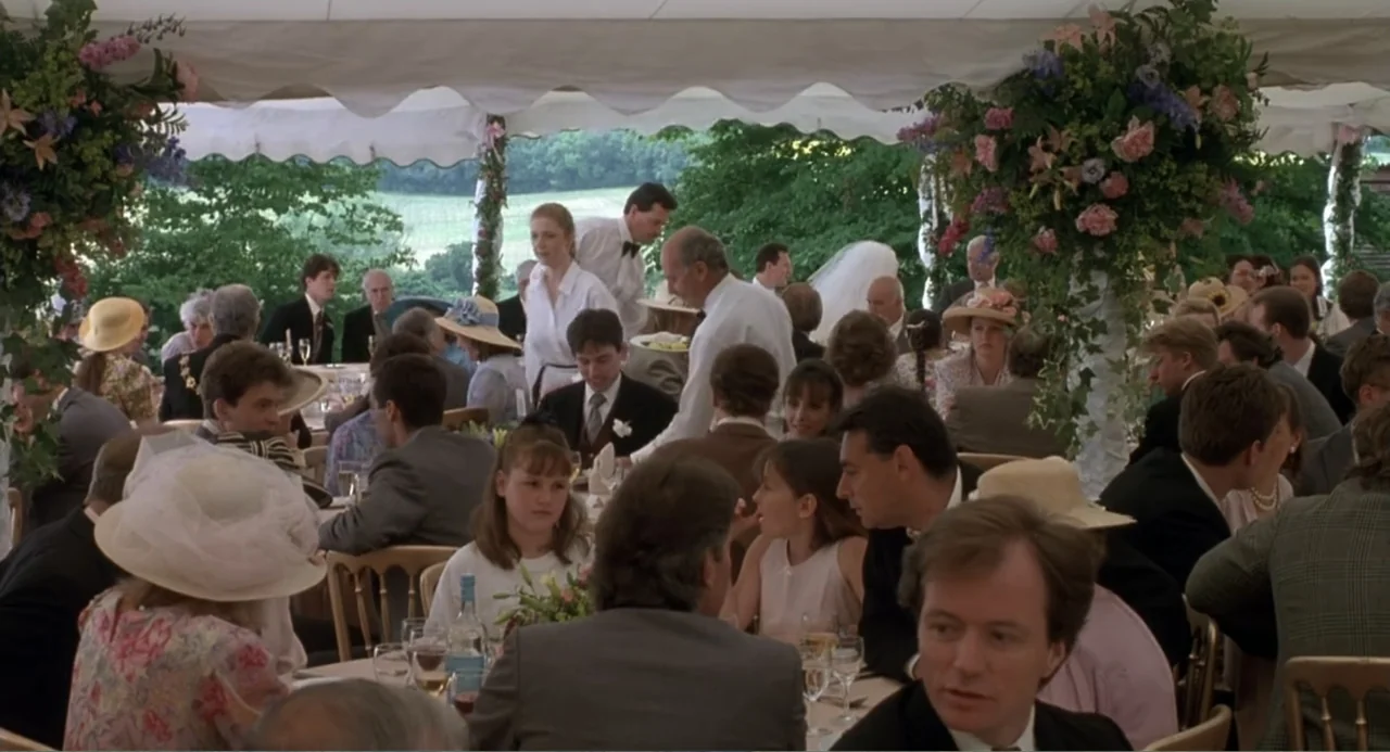 Four Weddings and a Funeral (1994) movie still: wide — A crowded white marquee tent hosts a wedding reception with guests seated at round tables. A…