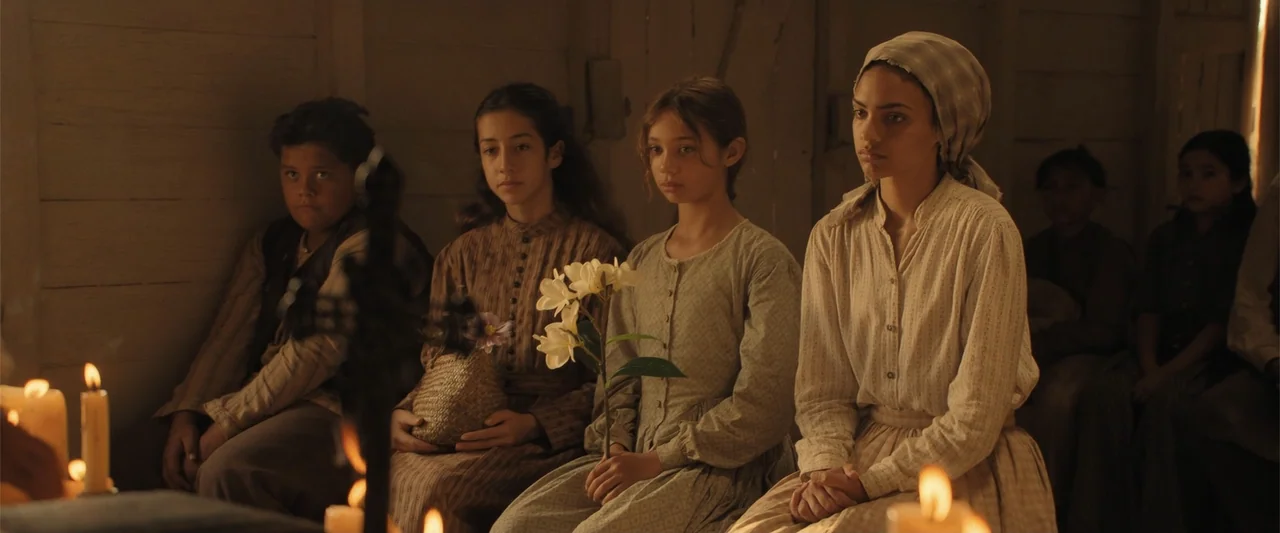 The Bluff (2026) movie still: medium — An interior wooden room contains several children sitting together on a bench. They sit side-by-side facing…