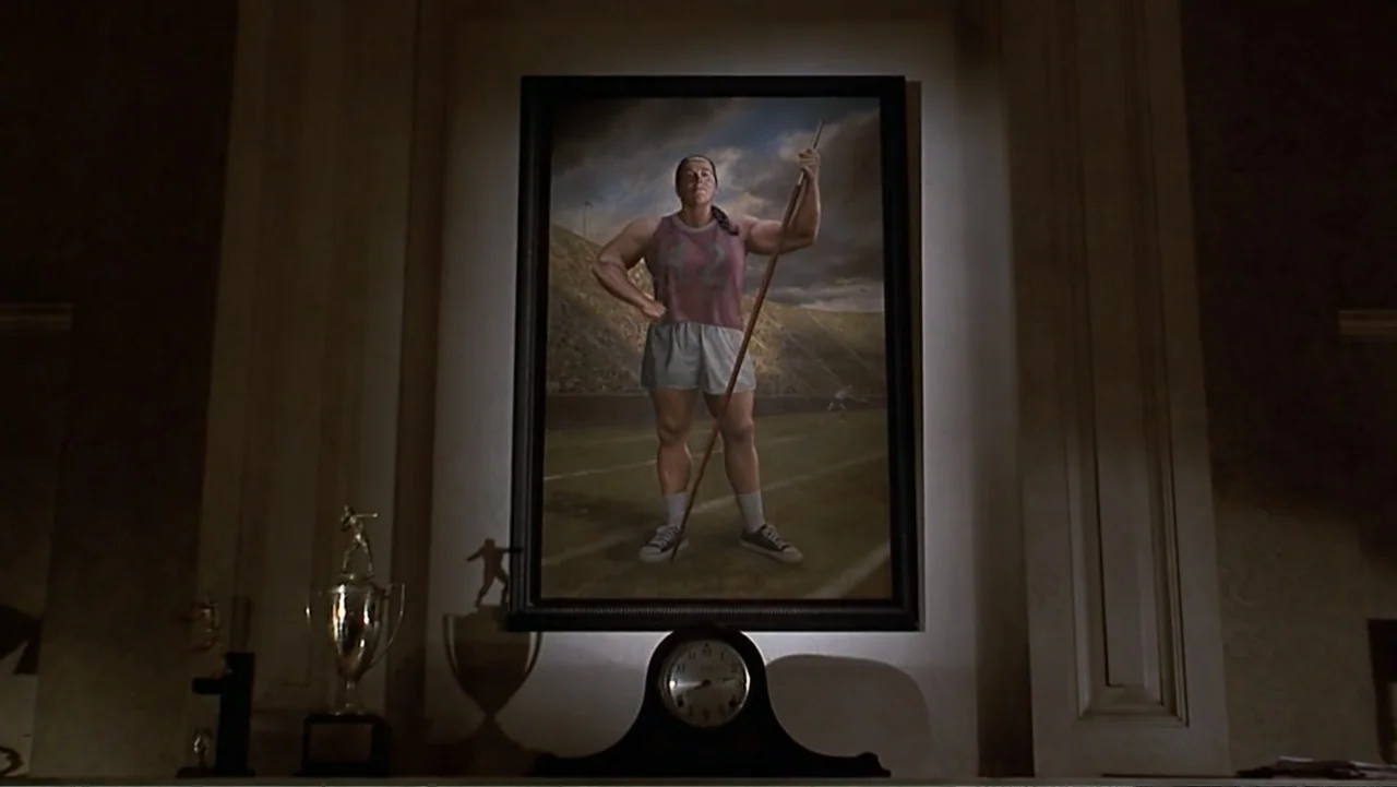 Matilda (1996) movie still: medium — A framed portrait of a female athlete hangs above a wooden fireplace mantel. An analog mantle clock sits…