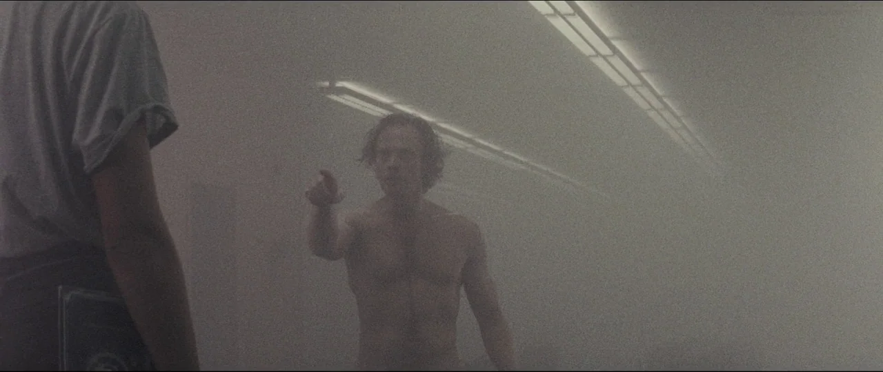 Luz (2018) movie still: medium — A locker room interior is obscured by a thick, heavy haze of smoke. A shirtless man stands facing another person,…