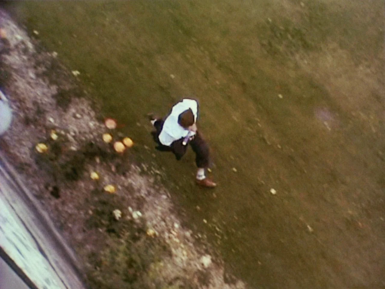 Festen (1998) movie still: wide — A person runs across a patch of green grass in an outdoor area. The perspective is a high angle, looking down from…