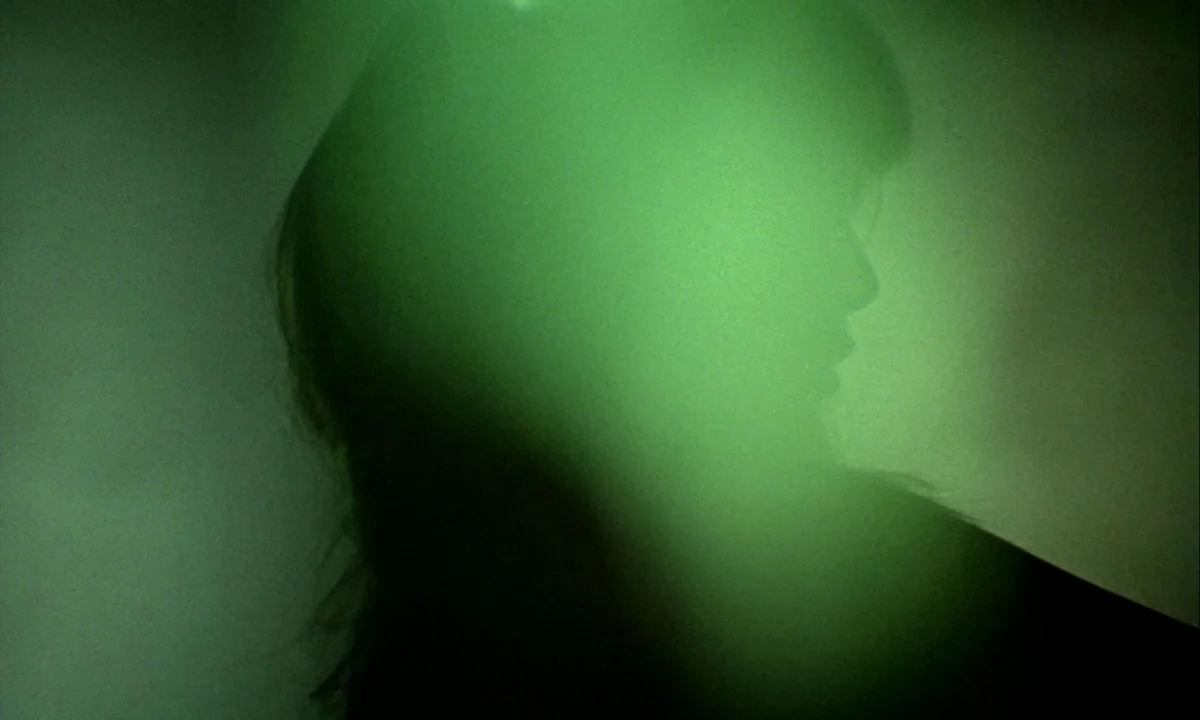 Wonderwall (1968) movie still: closeup — An abstract, dimly lit space is filled with a bright green atmospheric glow. A person is visible in…