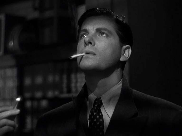 Saboteur (1942) movie still: closeup — A dark study filled with bookshelves stands in the background behind the main subject. The man looks up…