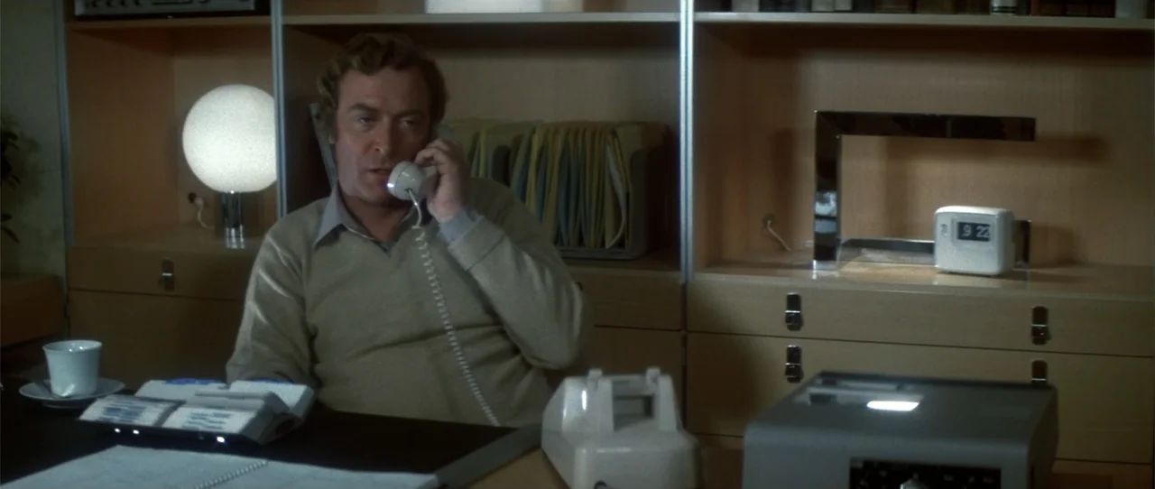 Dressed to Kill (1980) movie still: medium — A 1970s office with light-wood modular shelving units and modern desk equipment. A man sits at the desk…