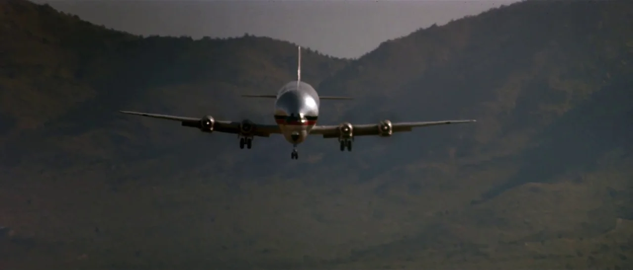 Universal Soldier (1992) movie still: wide — A silver passenger airplane approaches a landing strip against a backdrop of rolling hills. The…