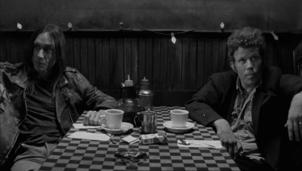 Coffee and Cigarettes (2003) movie still: medium — A dimly lit diner booth features a checkered table and simple wood-paneled walls. Two middle-aged…
