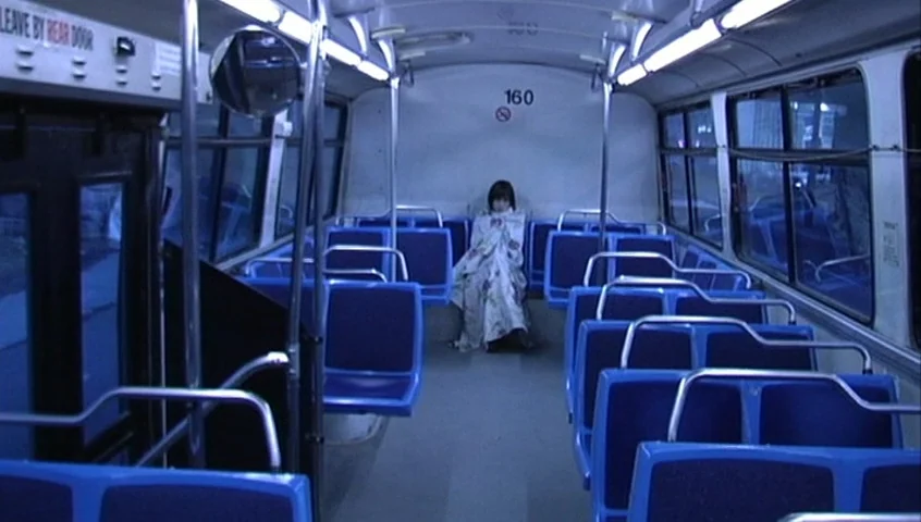 The Tracey Fragments (2007) movie still: wide — The interior of a city bus features rows of empty blue plastic seats. A young person sits alone on…