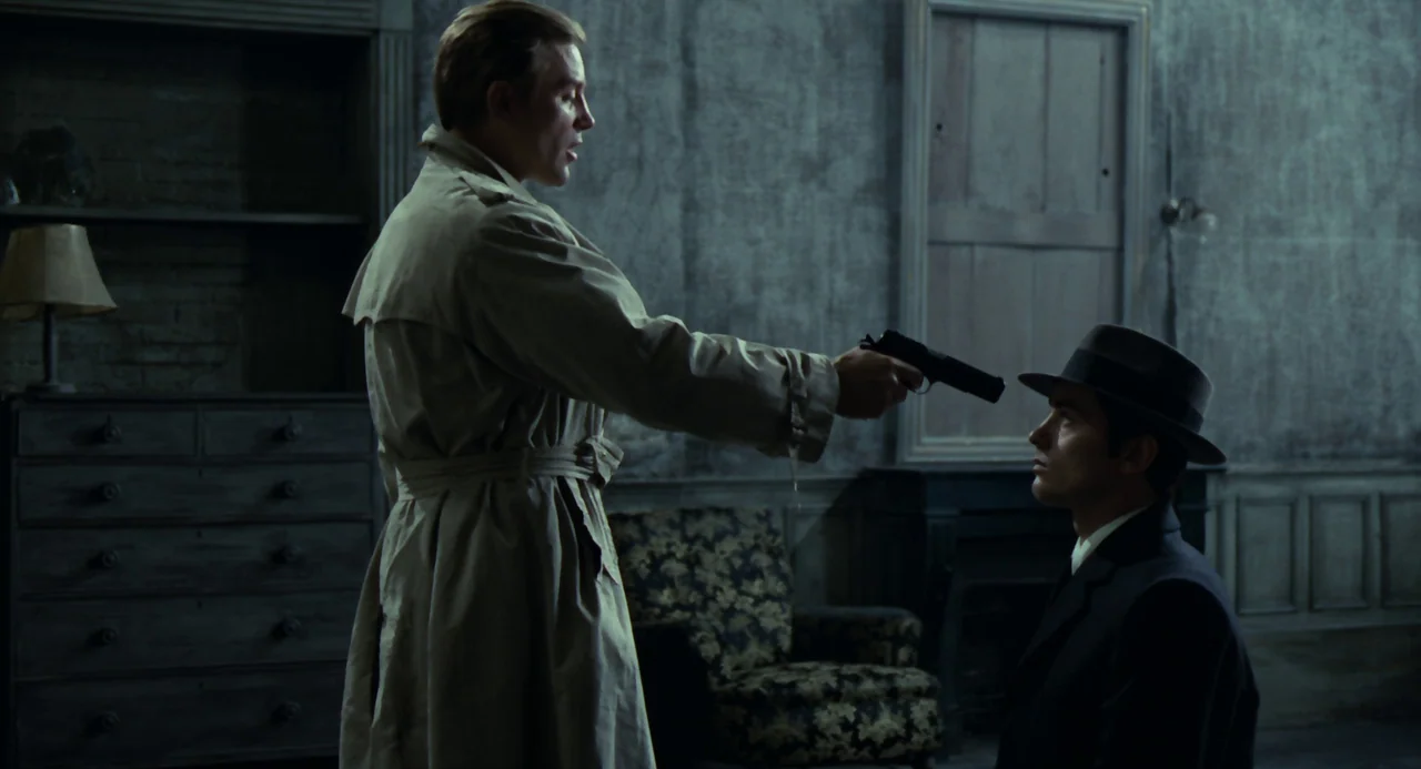 Le Samouraï (1967) movie still: medium — A dimly lit room with peeling grey wallpaper features a wooden dresser and armchair. One man stands…