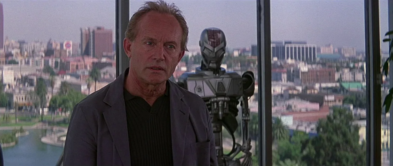 Scream 3 (2000) movie still: medium — A man stands inside a high-rise office with a sprawling cityscape visible through windows. Beside him stands a…