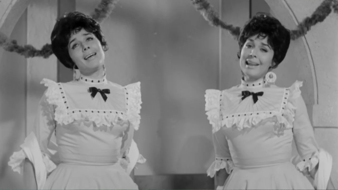 Escuela para solteras (1965) movie still: medium — A light-colored interior setting features draped decorative garlands framing two identical women…