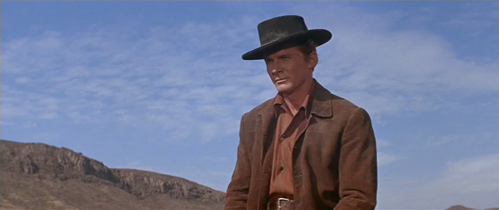 Flaming Star (1960) movie still: medium — A man stands outdoors in a dry, mountainous desert environment under a bright sky. The subject wears a…