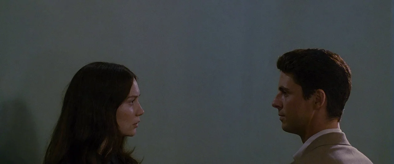 Stoker (2013) movie still: medium — A man and a woman stand facing each other in a dimly lit, minimalist room. The figures are captured in profile…