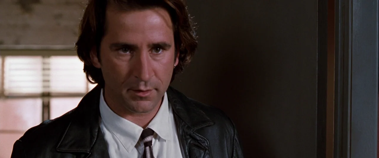 Empire Records (1995) movie still: closeup — A man stands in an interior space with a window visible in the background. The subject is positioned…