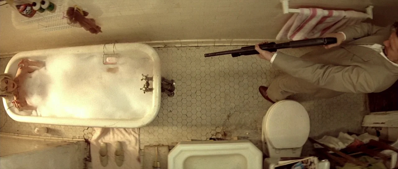 Léon: The Professional movie still: wide — A cramped tiled bathroom with a vintage clawfoot tub filled with white soap foam. A man in a light tan…