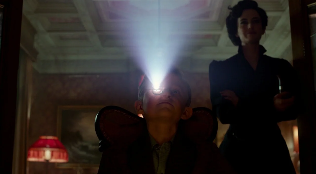 Miss Peregrine’s Home for Peculiar Children (2016) movie still: medium — A dimly lit room with patterned wallpaper features a young boy seated in a…