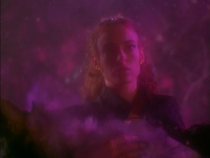 Twilight of the Ice Nymphs (1997) movie still: medium — A woman stands in a dark, hazy outdoor environment illuminated by saturated magenta light.…