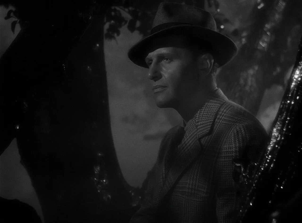 The Wolf Man (1941) movie still: medium — A man stands outdoors among dark trees at night in a film noir style. He stares ahead into the darkness…