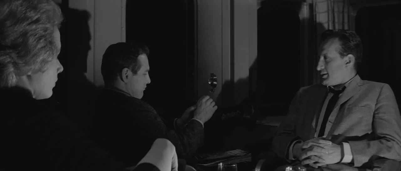 The Hustler (1961) movie still: medium — A dimly lit train compartment with dark windows and patterned fabric seating at night. Three people are…