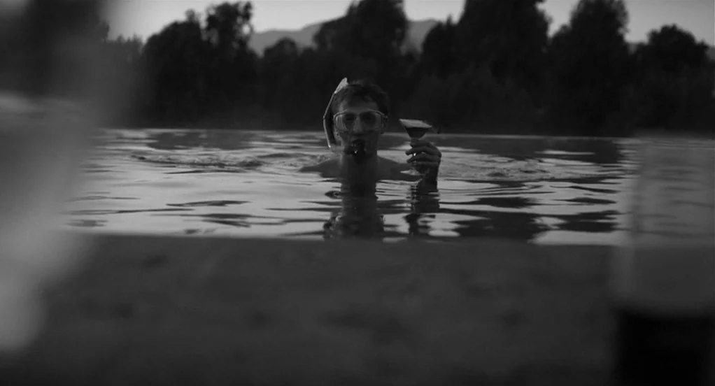 Much Ado About Nothing (2012) movie still: medium — A man wearing a diving mask and snorkel swims in a dark water pool. He holds a martini glass in…