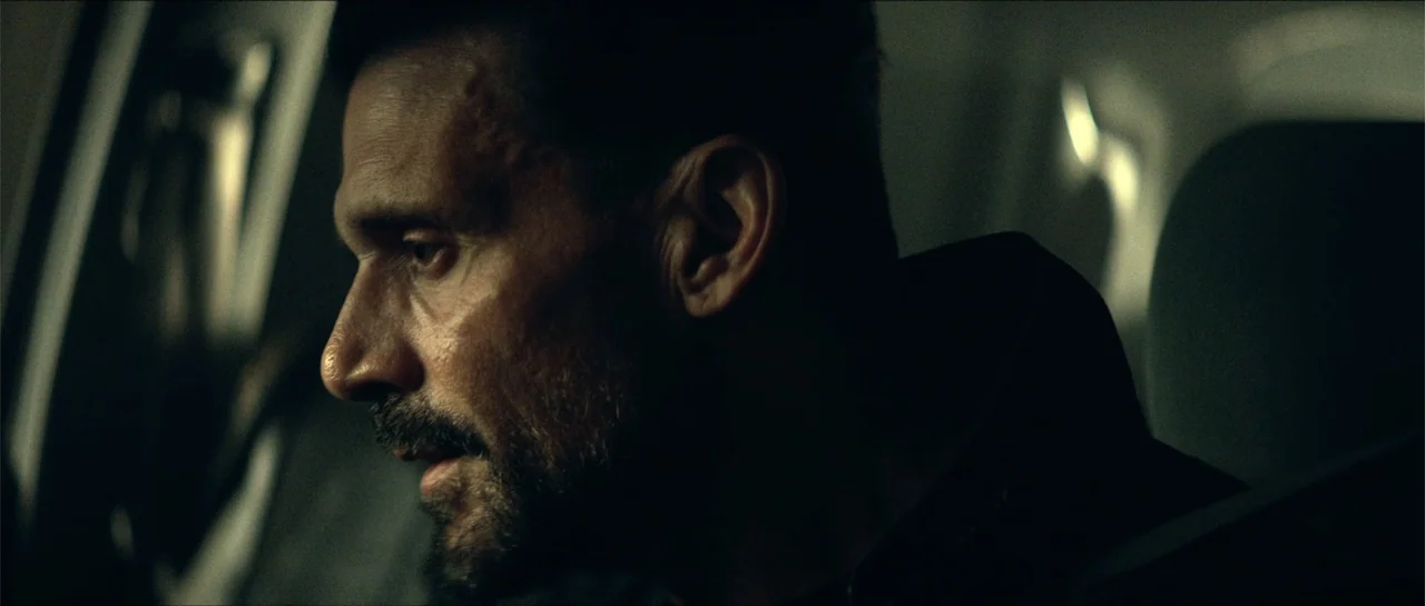 Cosmic Sin (2021) movie still: closeup — The interior of a car at night is dark with minimal ambient light. A man with a beard sits in the seat…