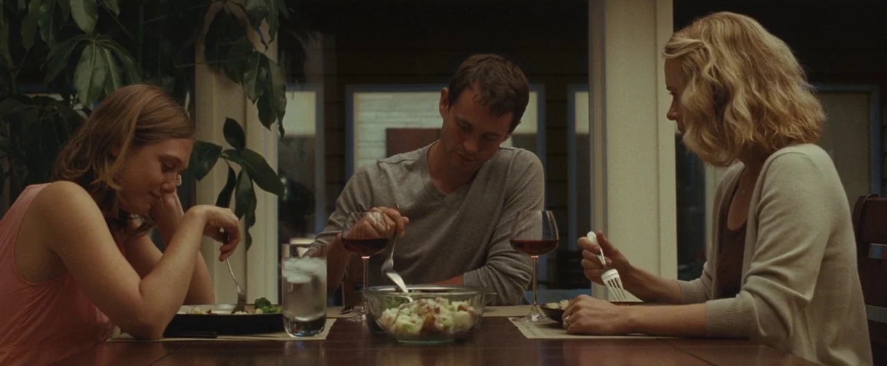 Martha Marcy May Marlene (2011) movie still: medium — A residential dining area features a wooden table with place settings and food. Three adults…