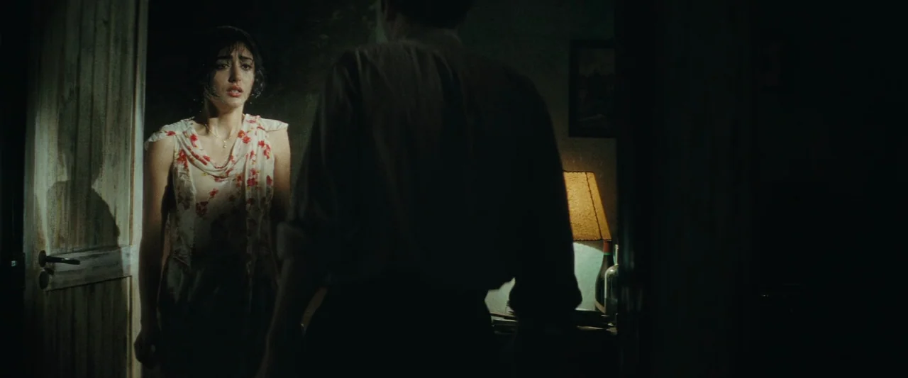 Chicken With Plums (2011) movie still: medium — A dimly lit passage features a woman standing by a wooden doorway. A man faces away from the camera…