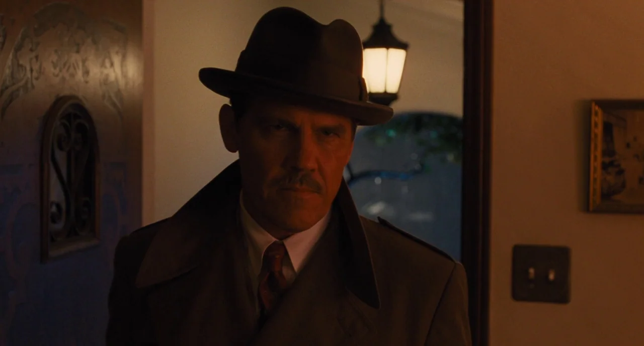 Hail, Caesar! (2016) movie still: medium — A dimly lit residential foyer features a dark wooden door and a wall-mounted light switch. A man in a…