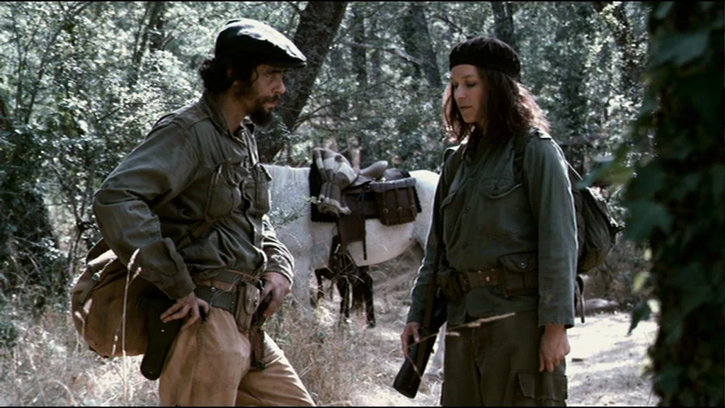 Che Part 2 (Guerrilla) (2008) movie still: medium — A dense forest clearing contains a saddled horse and two soldiers in military fatigues. The man…