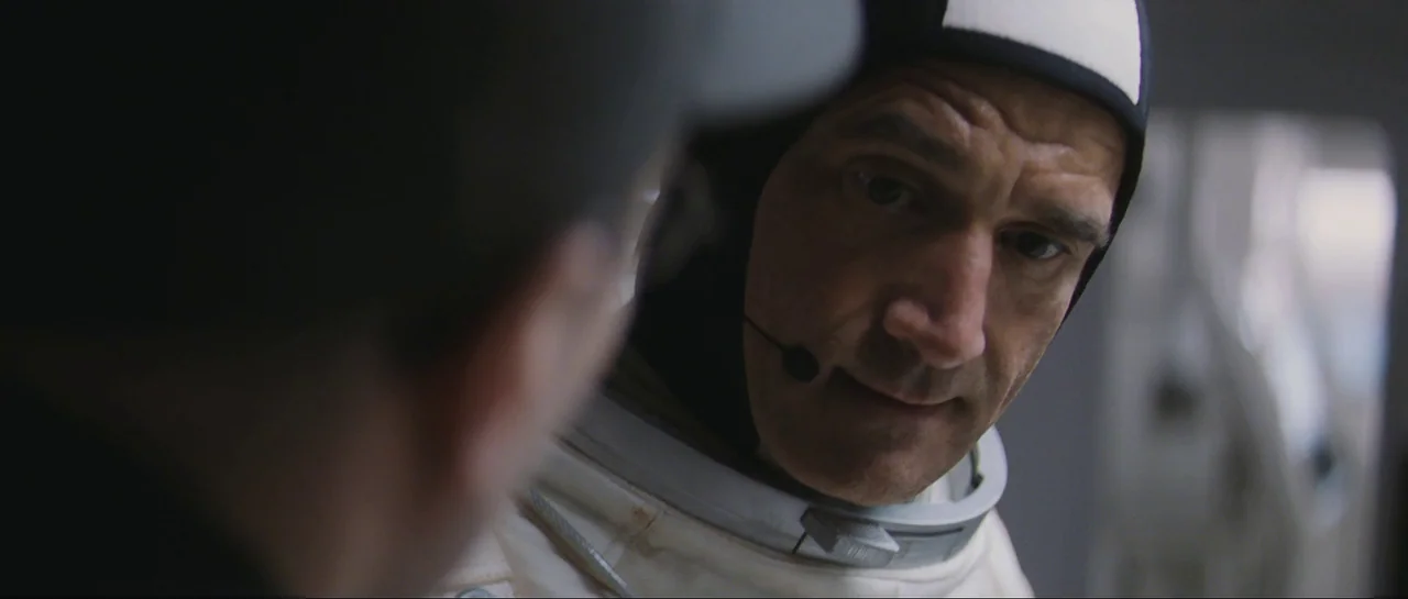 The Last Days On Mars (2013) movie still: closeup — A dimly lit spacecraft interior with metallic panels and white flight gear. An astronaut with a…
