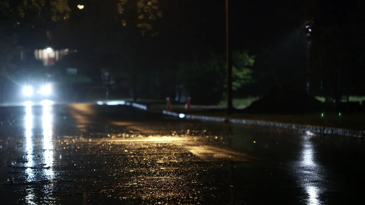 Breslin and Hamill: Deadline Artists (2018) movie still: wide — An asphalt road surface at night with rain puddles reflecting artificial light…