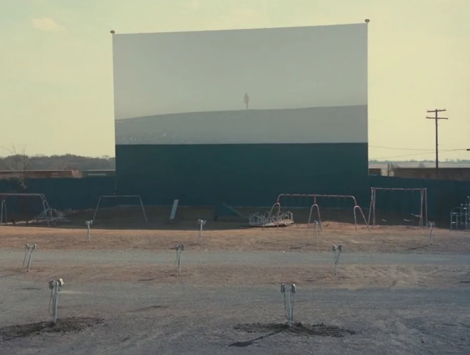 The Other Side of the Wind (2018) movie still: wide — An abandoned outdoor drive-in theater features a large, blank screen behind a playground. Rows…
