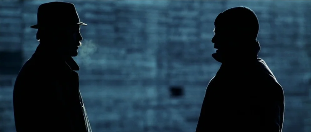 Confessions of a Dangerous Mind (2002) movie still: medium — Two men stand before a textured, industrial concrete surface during a cold night. They…
