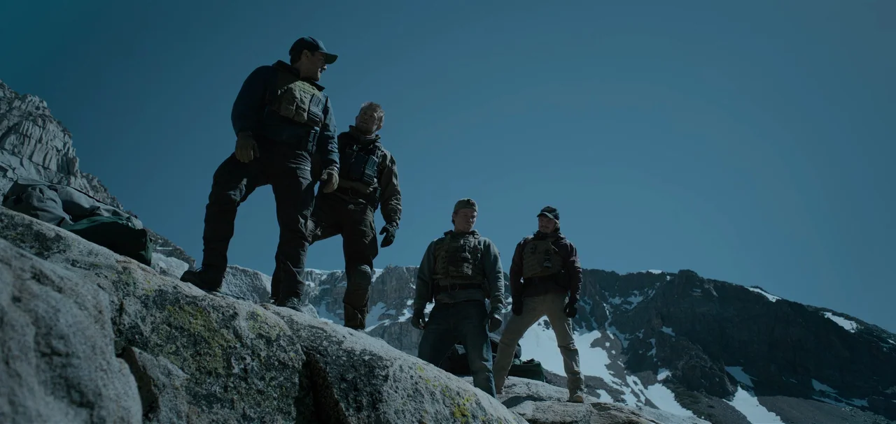 Triple Frontier (2019) movie still: fullbody — A group of four men in tactical gear stand on a rocky mountain slope. Snow-capped peaks rise in the…