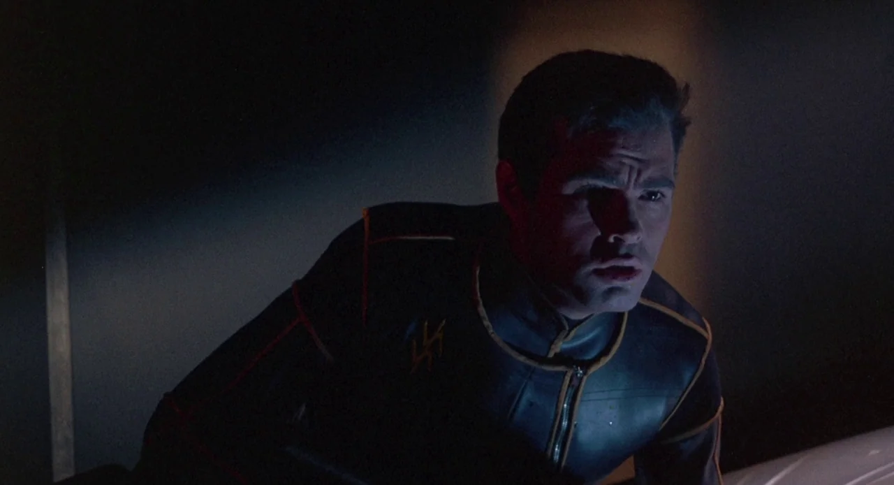 Planet of the Vampires (1965) movie still: medium — A dimly lit interior space with deep shadows surrounding the main subject. The man leans forward…