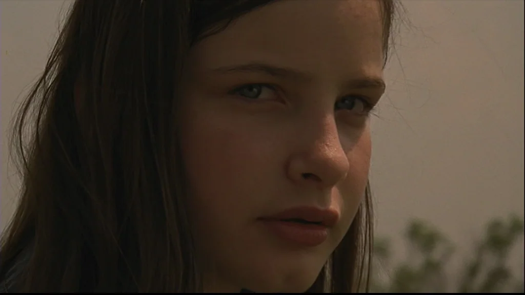 Margot At The Wedding (2007) movie still: closeup — A close-up view of a young woman against a blurred natural outdoor background. She looks toward…