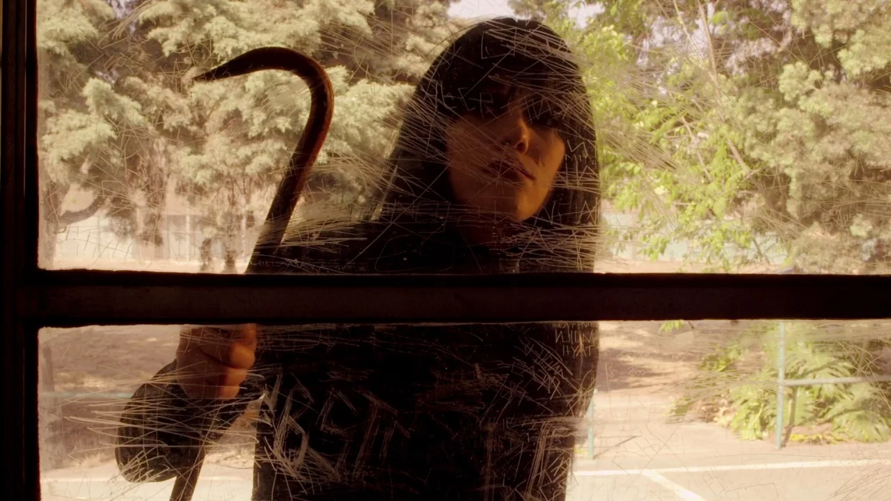Suburban Gothic (2014) movie still: medium — A woman looks through the heavily scratched and etched glass of a vehicle window. She holds a rusted…