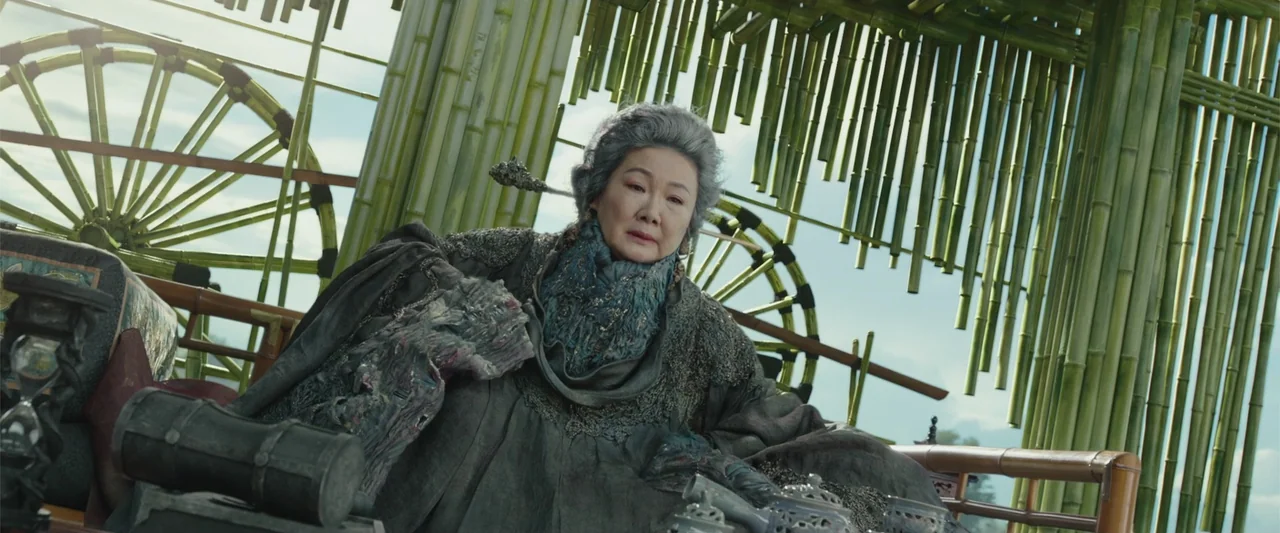 Along with the Gods: The Two Worlds (2017) movie still: medium — An elderly woman sits inside a structure built from green bamboo poles and wheels.…