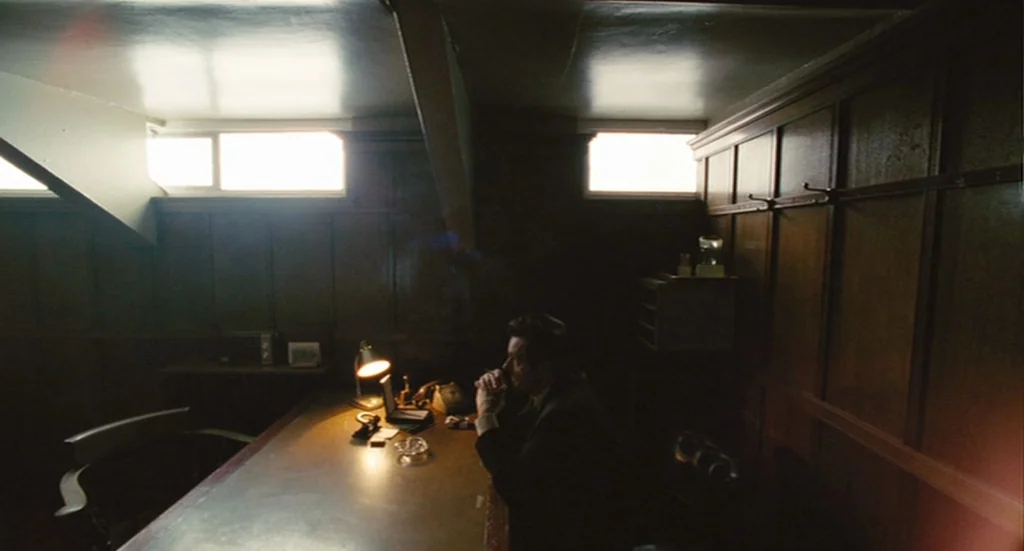 The Damned United (2009) movie still: wide — An office with wood paneled walls features two high rectangular windows letting in daylight. A man sits…
