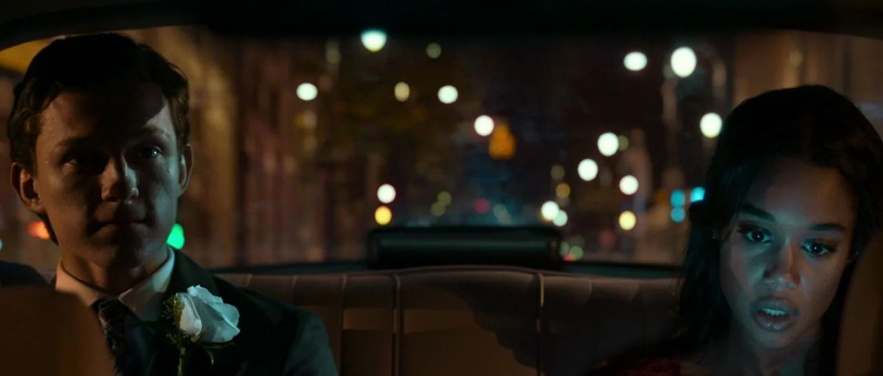 Spider Man: Homecoming (2017) movie still: medium — The back seat of a moving vehicle at night with blurred city lights behind. A young man and…
