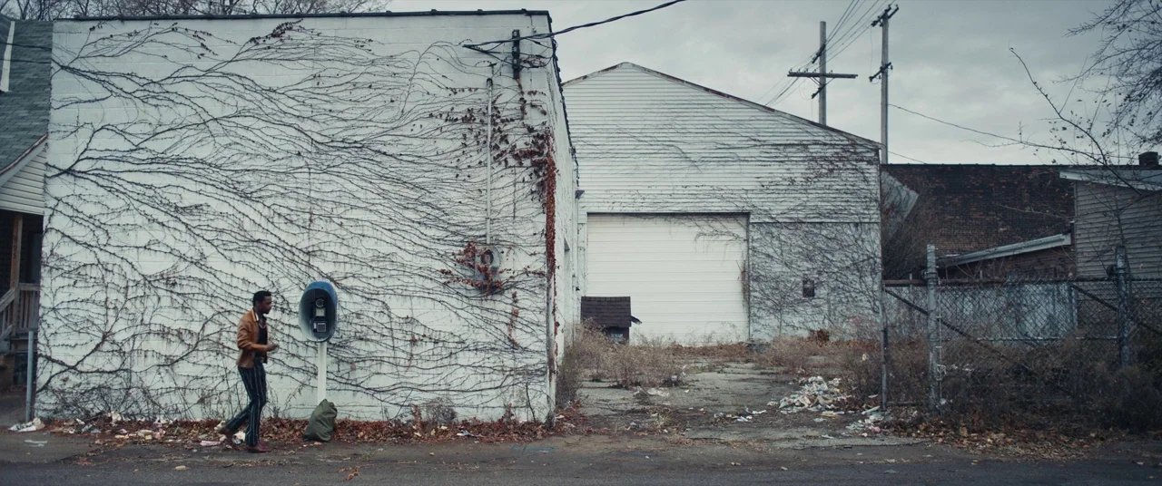 Judas and the Black Messiah (2021) movie still: wide — An urban setting with a white industrial building covered in dry, dead climbing vines. A lone…