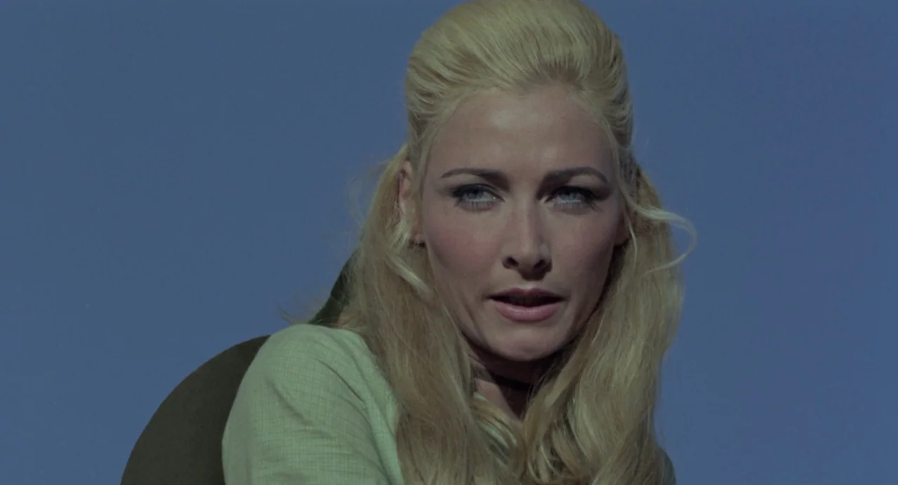 Johnny Colt (1966) movie still: closeup — A woman stands in front of a vast, cloudless blue sky backdrop. She looks toward the side of the frame…