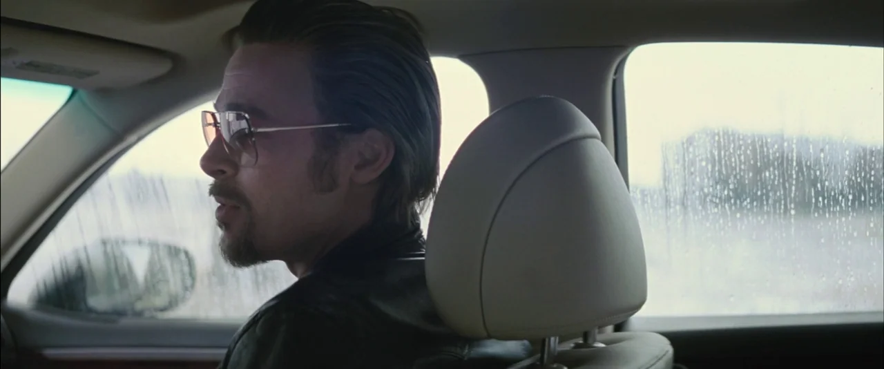 Killing Them Softly (2012) movie still: medium — Interior of a moving car during a rainstorm on a cloudy day. A man with a goatee and slicked hair…