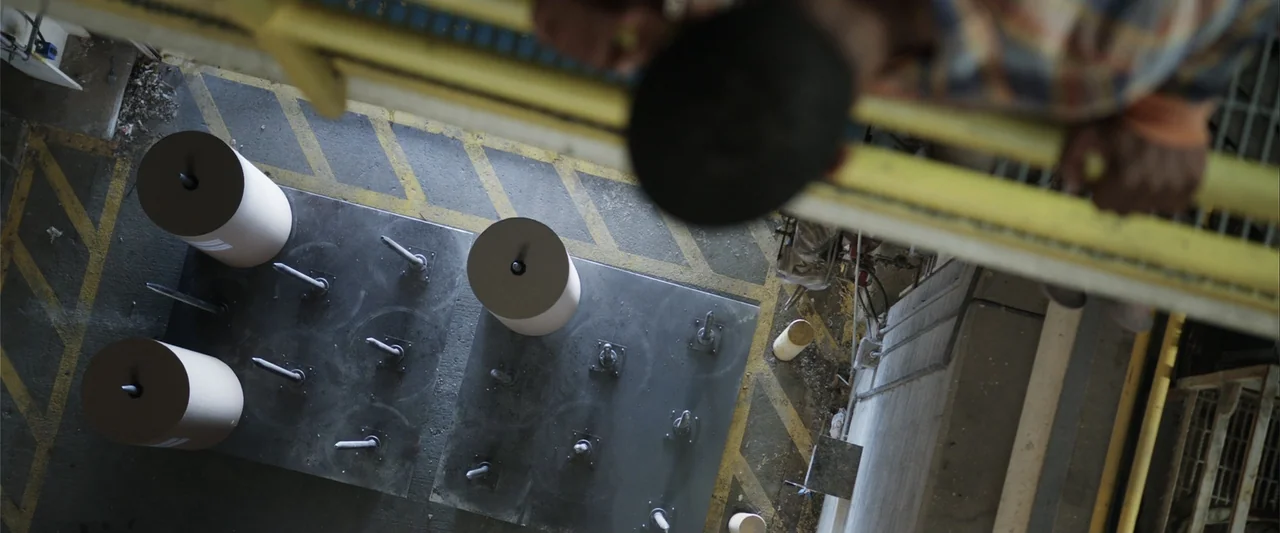 Final Destination 5 (2011) movie still: wide — An industrial floor features metal plates with white cylindrical objects arranged in rows. Yellow…