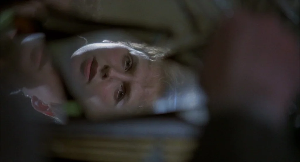 Brazil (1985) movie still: closeup — A dark indoor space features a person resting their head on a flat surface. The soft light highlights the face…