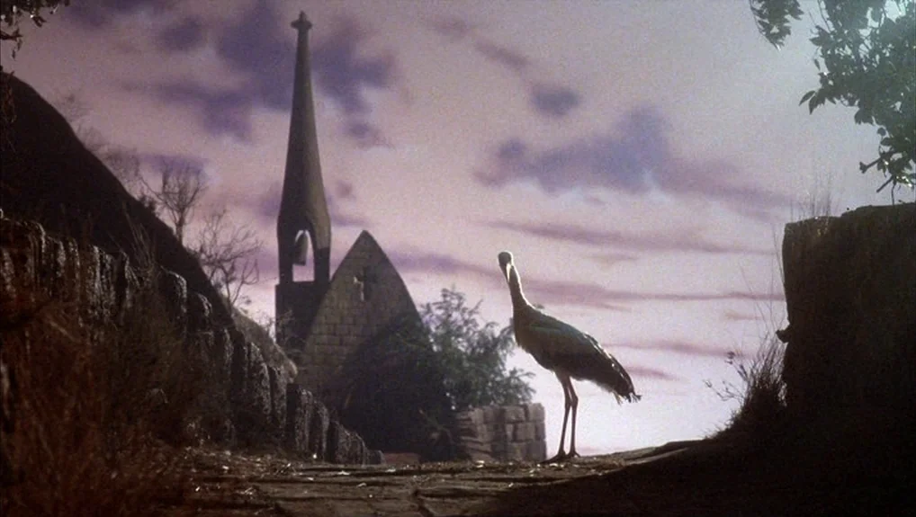 The Company of Wolves (1984) movie still: wide — A stone pathway leads past a dark, silhouetted stone church with a tall steeple. A single heron…