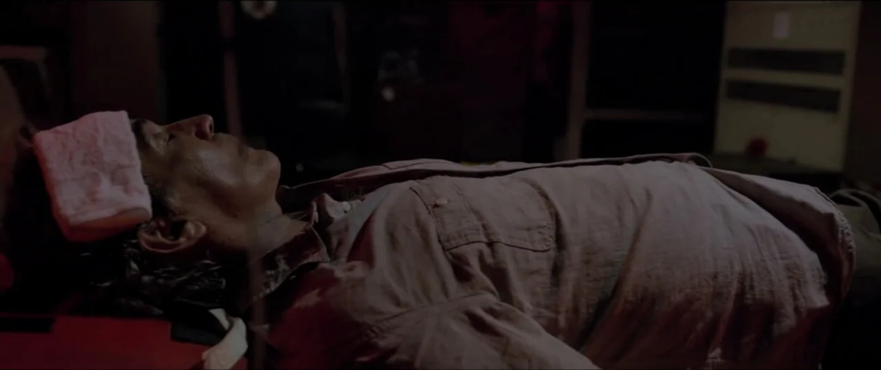 Primal (1994) movie still: medium — An interior bedroom at night with dark shadows surrounding a person resting on a bed. A middle-aged man with a…