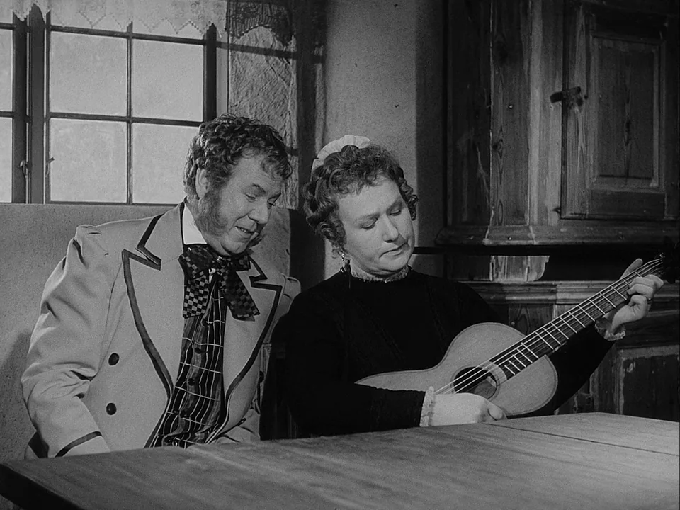 The Magician (1958) movie still: medium — An interior space with a wooden table, rough walls, and a small window nearby. A middle-aged woman plays a…