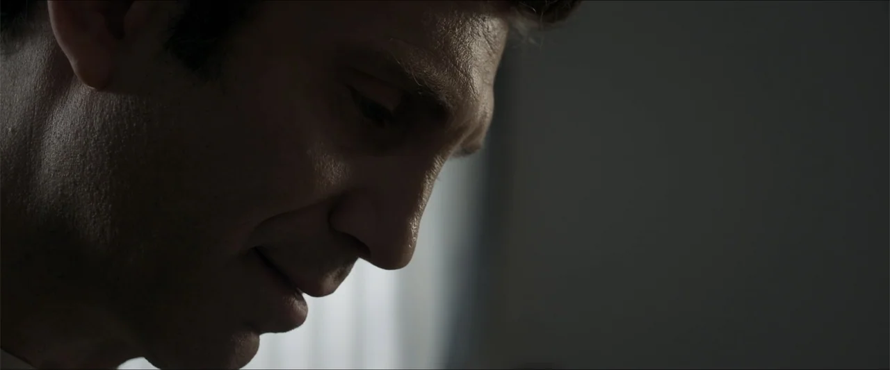 Heavenly Deposit (2019) movie still: closeup — An interior space is dimly lit by light filtering from a nearby window. A man stands in the frame…